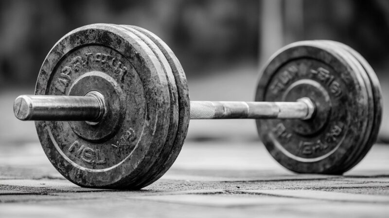 A black and white image of a heavy barbell resting on the gym floor, showing signs of wear and use